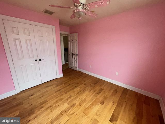 unfurnished bedroom featuring baseboards, visible vents, a ceiling fan, wood finished floors, and a closet