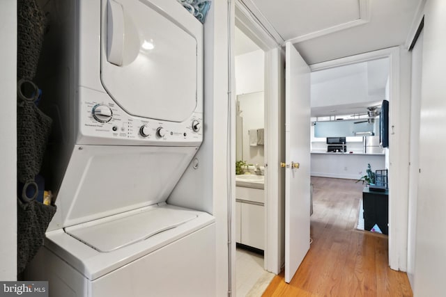 laundry area with a sink, light wood-style floors, laundry area, and stacked washer / drying machine