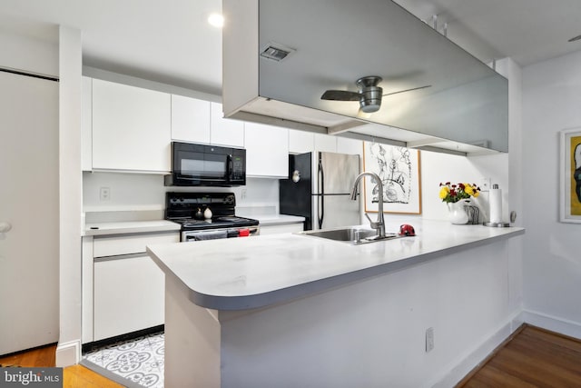 kitchen with light countertops, white cabinets, a sink, a peninsula, and black appliances