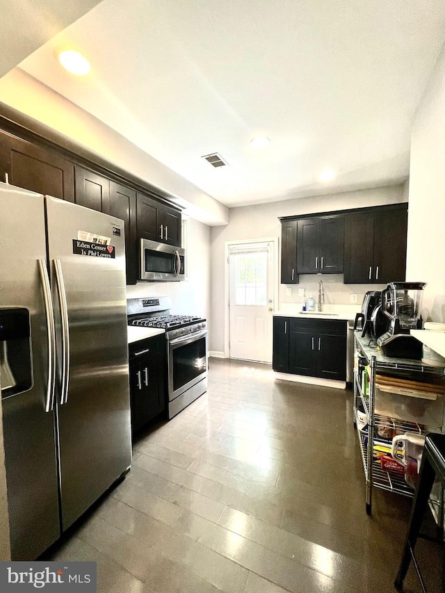 kitchen featuring light countertops, visible vents, appliances with stainless steel finishes, a sink, and dark cabinetry