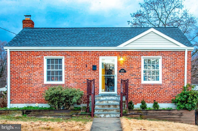 bungalow-style house featuring brick siding, a chimney, and a shingled roof