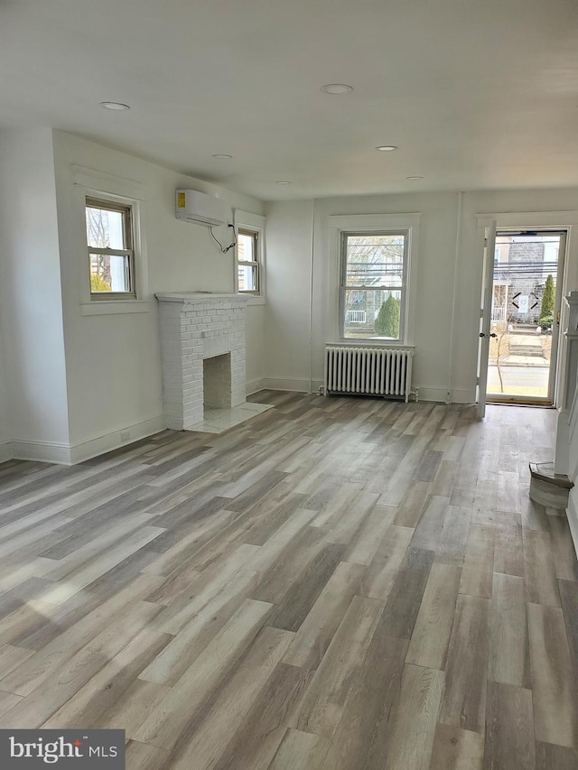 unfurnished living room with radiator, a fireplace, wood finished floors, and a wall mounted air conditioner