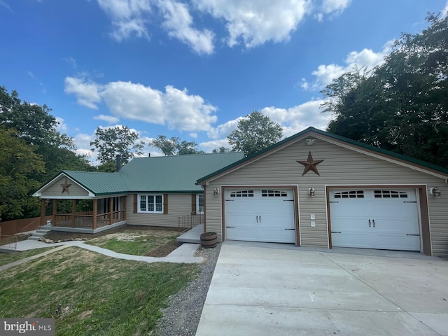 view of front of property featuring metal roof, a porch, an attached garage, driveway, and a front yard