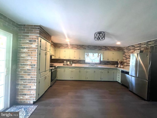 kitchen featuring stainless steel appliances, dark wood-type flooring, brick wall, a sink, and light countertops