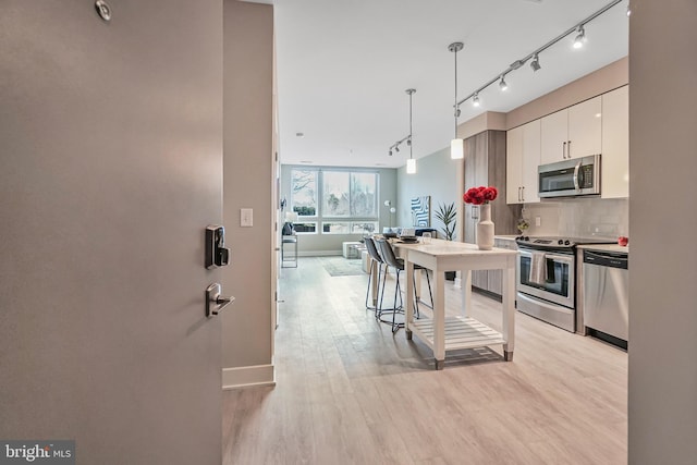 kitchen with stainless steel appliances, white cabinetry, hanging light fixtures, light wood-type flooring, and backsplash