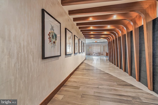 corridor featuring beamed ceiling, baseboards, and wood finished floors