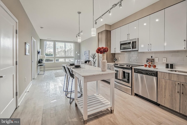 kitchen featuring tasteful backsplash, hanging light fixtures, stainless steel appliances, light countertops, and light wood-type flooring