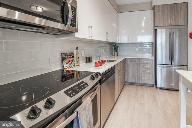 kitchen featuring stainless steel appliances, light countertops, backsplash, a sink, and modern cabinets