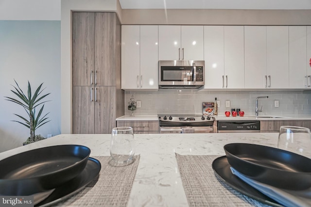 kitchen featuring light stone counters, stainless steel appliances, a sink, white cabinetry, and tasteful backsplash