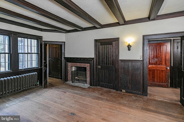 unfurnished living room with a wainscoted wall, beamed ceiling, radiator heating unit, and hardwood / wood-style flooring