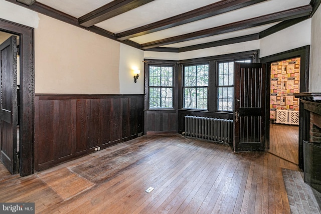 spare room with beam ceiling, wainscoting, hardwood / wood-style floors, and radiator heating unit