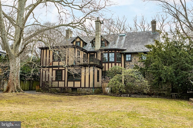 rear view of house featuring a lawn, a sunroom, stone siding, a chimney, and a high end roof