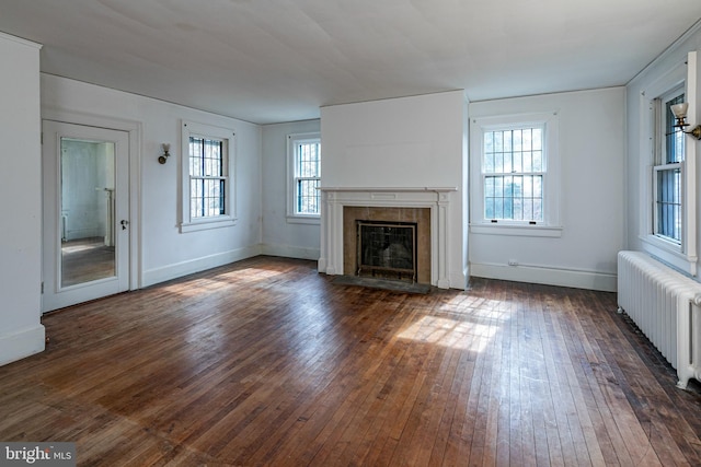 unfurnished living room featuring dark wood-type flooring, a fireplace with flush hearth, baseboards, and radiator heating unit