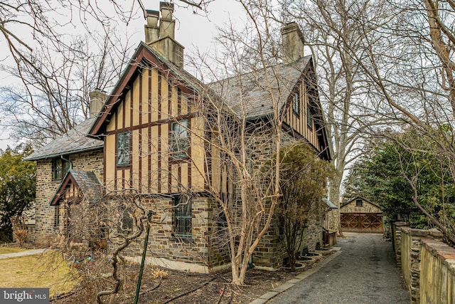 view of side of home featuring a high end roof, stone siding, and a chimney