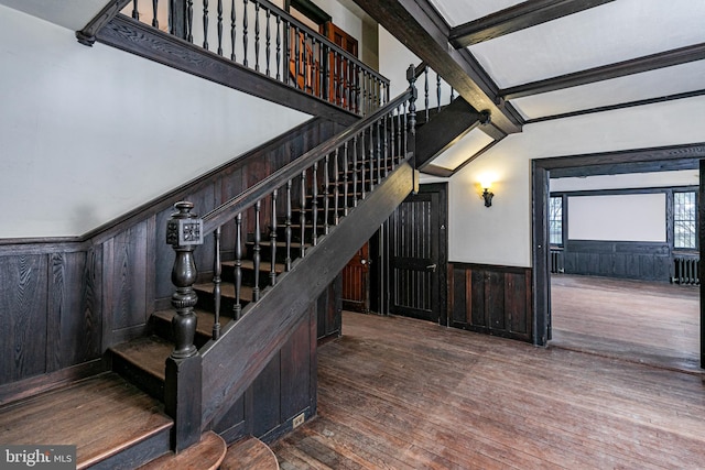 stairway featuring wood walls, beamed ceiling, hardwood / wood-style floors, and wainscoting