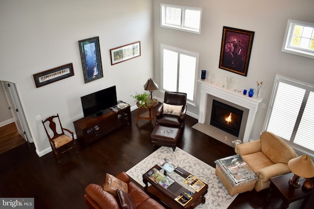 living area with a towering ceiling, a fireplace with flush hearth, baseboards, and wood finished floors