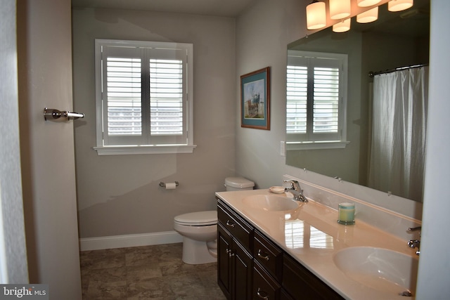 bathroom featuring toilet, double vanity, baseboards, and a sink