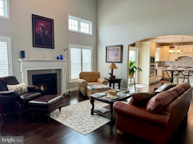 living room featuring a towering ceiling, a fireplace, arched walkways, and dark wood finished floors