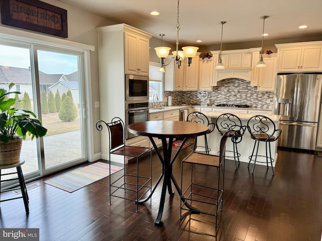 kitchen with stainless steel appliances, dark wood finished floors, hanging light fixtures, tasteful backsplash, and a kitchen bar