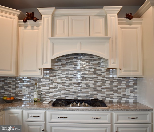 kitchen with premium range hood, stainless steel gas stovetop, white cabinetry, and backsplash