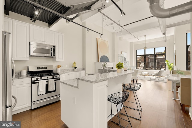 kitchen with stainless steel appliances, wood finished floors, light stone countertops, and white cabinets