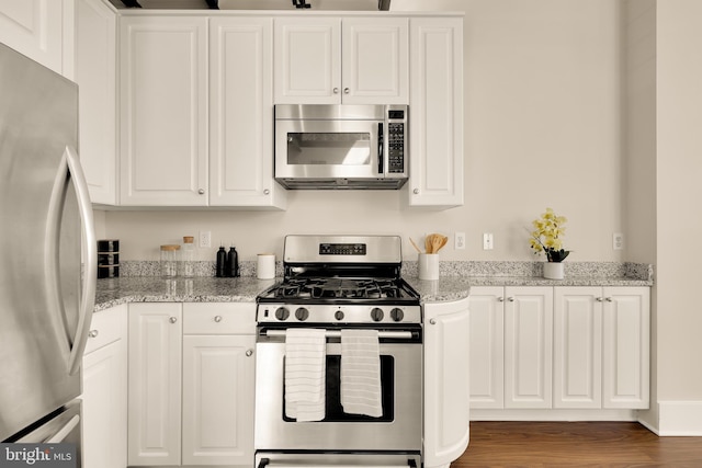 kitchen with stainless steel appliances, light stone countertops, white cabinets, and wood finished floors