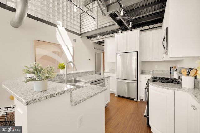 kitchen with stainless steel appliances, a high ceiling, white cabinets, a sink, and wood finished floors