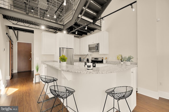 kitchen featuring stainless steel appliances, a breakfast bar, a towering ceiling, white cabinets, and light wood finished floors