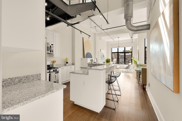 kitchen with appliances with stainless steel finishes, dark wood-type flooring, a kitchen bar, and white cabinetry