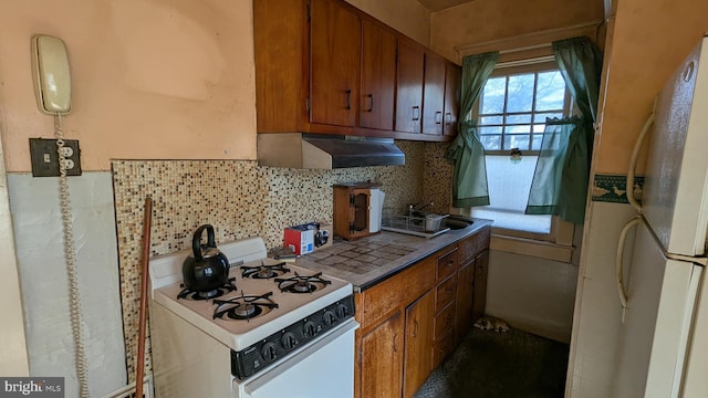 kitchen featuring white appliances, under cabinet range hood, brown cabinetry, and a sink