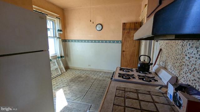 kitchen featuring cooktop, under cabinet range hood, baseboards, and freestanding refrigerator