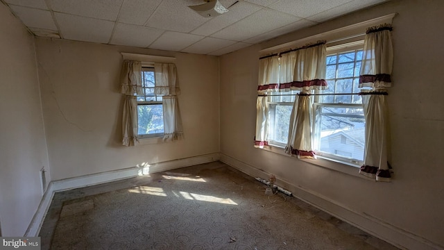 unfurnished room with plenty of natural light, a drop ceiling, and baseboards