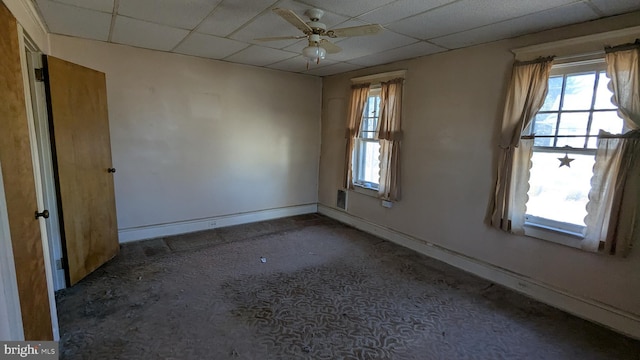 spare room with dark carpet, a drop ceiling, ceiling fan, and baseboards