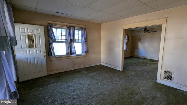 empty room with a ceiling fan, a drop ceiling, visible vents, and baseboards