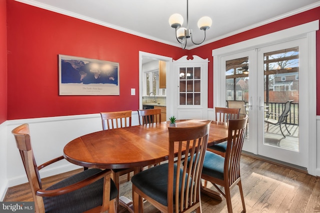 dining room featuring light wood-type flooring, french doors, a notable chandelier, and crown molding