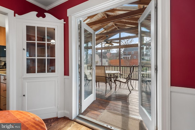 doorway to outside featuring ornamental molding, a wainscoted wall, vaulted ceiling, and wood finished floors