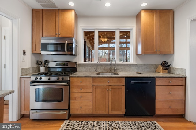 kitchen featuring light stone counters, light wood-style flooring, stainless steel appliances, a sink, and visible vents