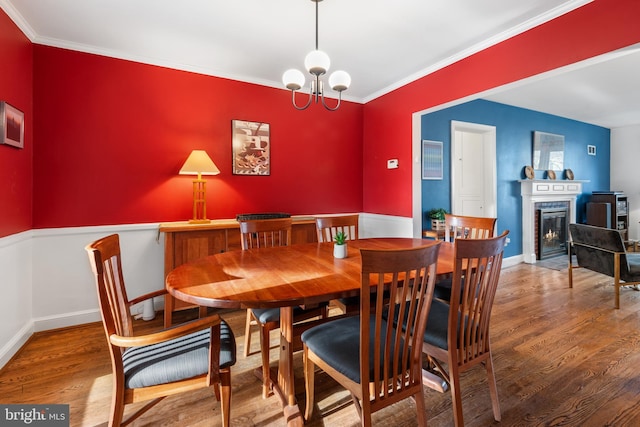 dining room with a fireplace with flush hearth, ornamental molding, wood finished floors, and an inviting chandelier