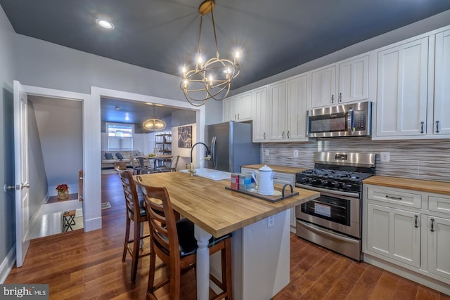 kitchen with dark wood-style floors, wooden counters, decorative backsplash, appliances with stainless steel finishes, and an island with sink