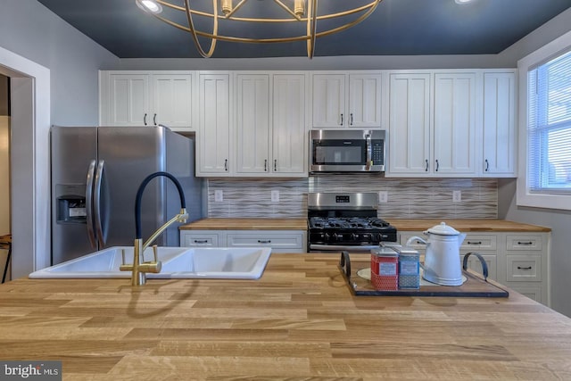 kitchen featuring tasteful backsplash, stainless steel appliances, white cabinetry, and wooden counters