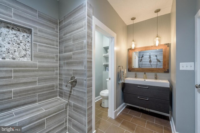 full bathroom with toilet, a tile shower, vanity, baseboards, and tile patterned floors