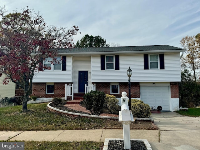 raised ranch with a garage, concrete driveway, and brick siding