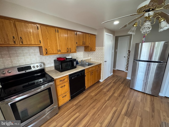 kitchen with brown cabinets, wood finished floors, light countertops, black appliances, and a sink