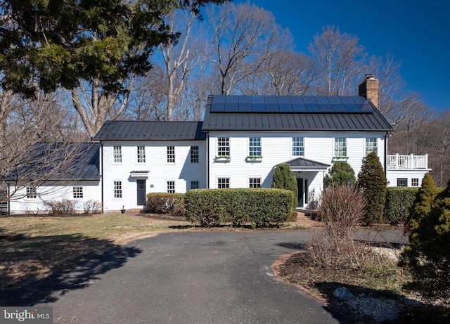 colonial-style house featuring a standing seam roof, metal roof, a chimney, and solar panels