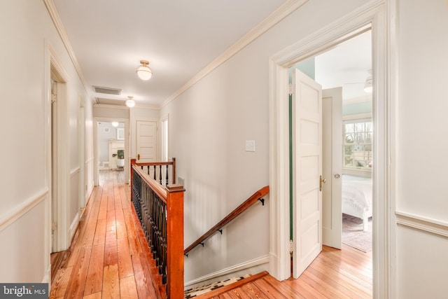 corridor with visible vents, ornamental molding, an upstairs landing, and light wood-style floors