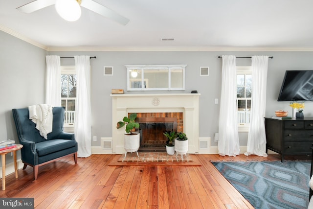 living area with ornamental molding, a brick fireplace, visible vents, and hardwood / wood-style flooring