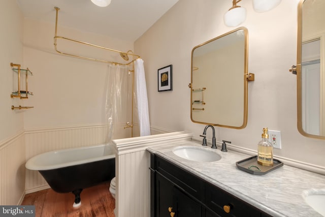 bathroom with double vanity, wainscoting, toilet, a soaking tub, and a sink