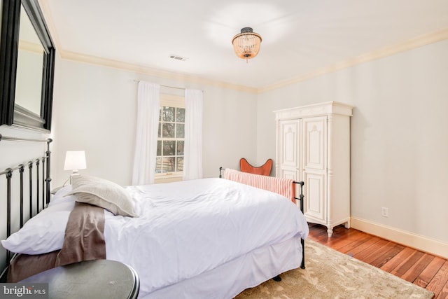 bedroom featuring hardwood / wood-style flooring, baseboards, visible vents, and ornamental molding