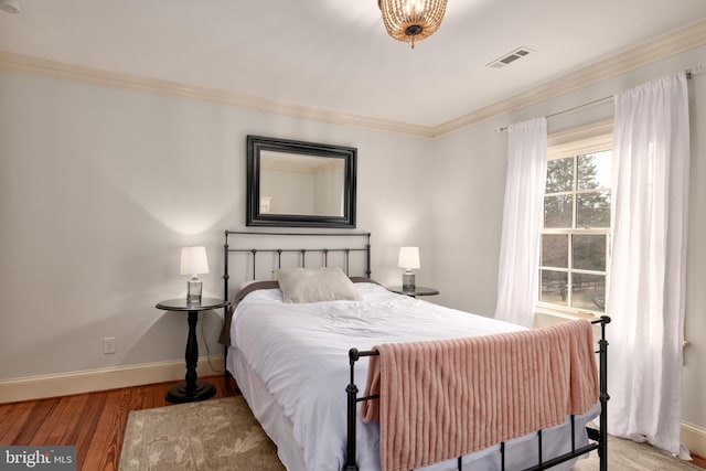 bedroom featuring baseboards, visible vents, wood finished floors, and ornamental molding