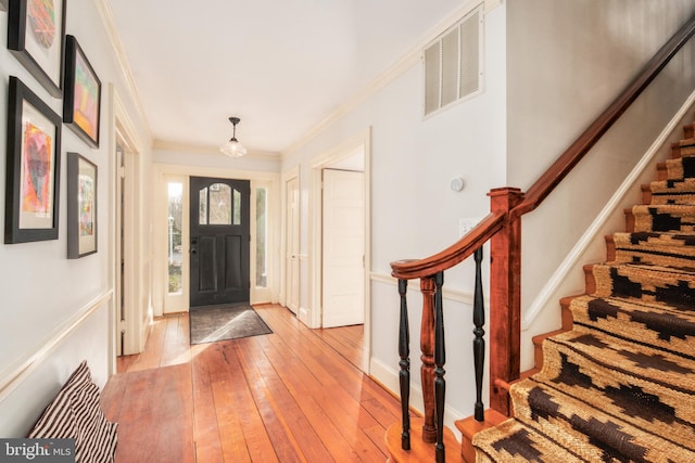 foyer entrance with baseboards, visible vents, ornamental molding, stairs, and light wood-style floors